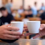 Cómo hablar de dinero sin arruinar la conexión Close-up of hands holding coffee cups during a business discussion, luxury café setting, soft focus