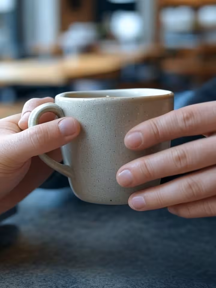 Close-up of hands holding coffee cup during serious conversation, blurred background showing café se